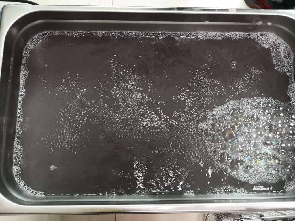Close-up of an ultrasonic cleaner tank filled with murky solution